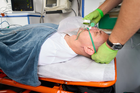 Man in protective gloves puts oxygen mask on patient in ambulance