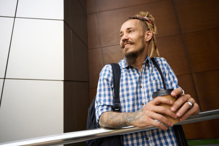 Happy man stands with glass of coffee outside modern buildingの写真素材