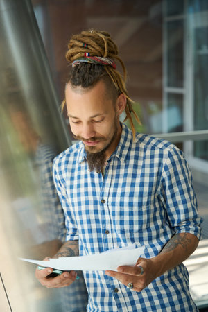 Guy is standing with papers and phone in front view windowの写真素材