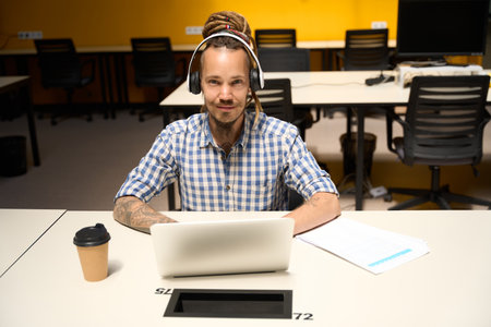 Informal man in plaid shirt sits with laptop at office desk