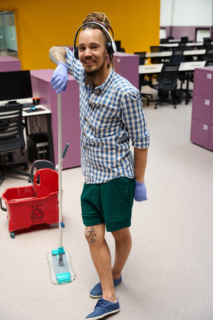 Happy informal standing in middle of coworking space with mop
