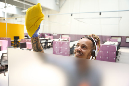 Cleaner in headphones rubs the transparent partition with yellow ragの写真素材