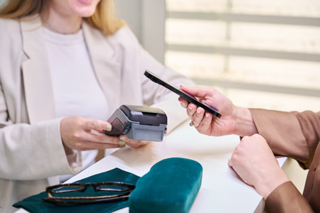 Woman in optics salon pays through terminal with mobile phoneの写真素材