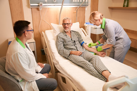 Caring nurse puts an IV on a gray-haired old man