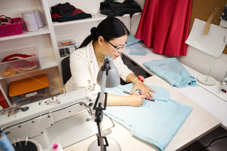 Sewing master at workplace works with blue fabricの写真素材