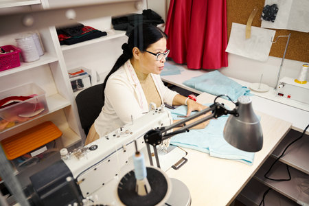 Experienced tailoring master at workplace working with blue fabric