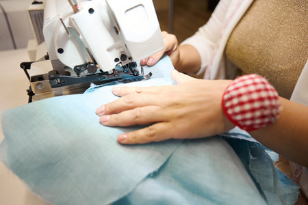 Lady works on a sewing machine with blue fabricの写真素材
