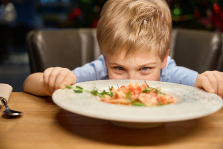 Funny little boy looking at plate with festive dish while celebrating New Yearの写真素材