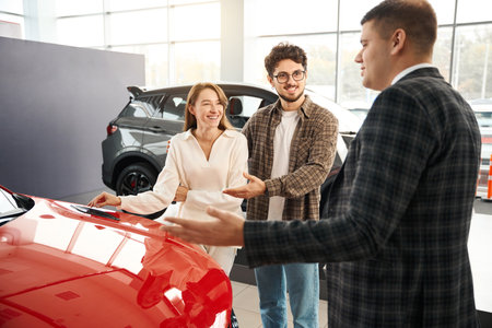Man and woman choosing and buying car at car showroom salesman helps them