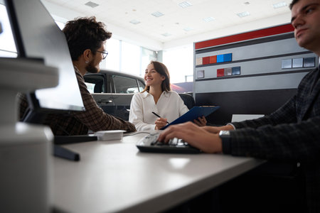 Auto salon seller helping man and woman customers choosing new car in dealershipの写真素材