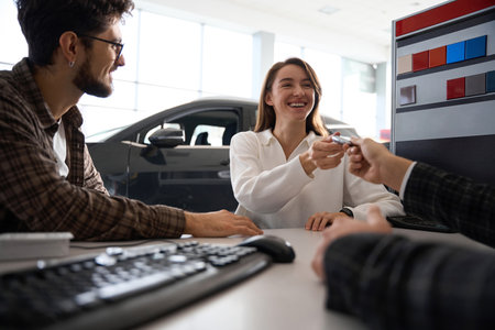 Woman taking keys of new car couple buying automobile sitting in office