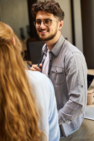 Smiling businessman looking at cropped businesswoman on table in officeの写真素材