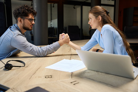 Concentrated businessman and businesswoman doing arm wrestling at desk in office