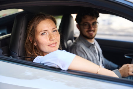Young smiling caucasian woman and blurred man looking at camera from car windowの写真素材