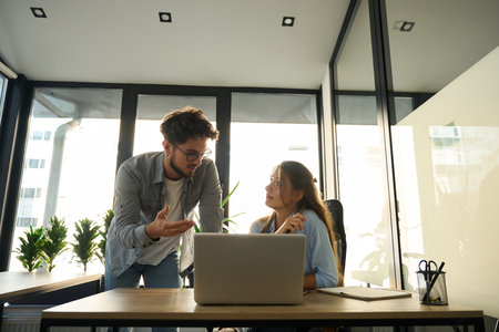 Businesswoman looking at male colleague while he showing something on laptop