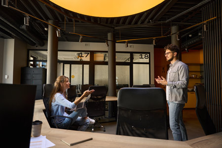 Side view of young serious businessman and businesswoman discussing during work