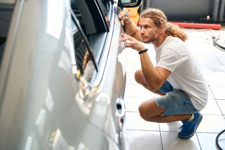Long-haired man smooths out dents on car door with straightening hammerの写真素材
