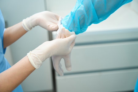 Partial image of female nurse helping male doctor put on latex glove on handの写真素材
