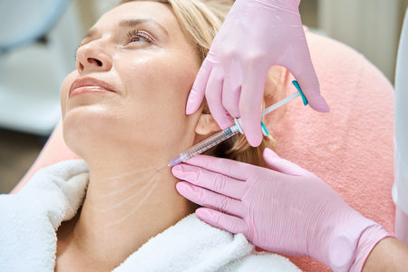 Cropped female beautician doing neck beauty injection with syringe of woman