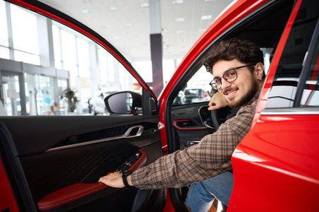 Man sitting in his new automobile cabin testing new car in dealershipの写真素材