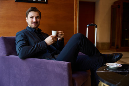 Cheerful man sitting and holding coffee cup in hands