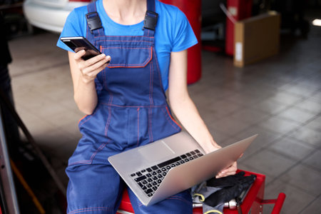 Female sits with laptop and mobile phone on red cabinetの写真素材