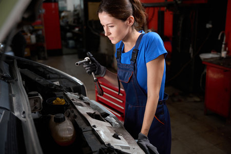 Woman in blue work clothes inspects engine under open hoodの写真素材