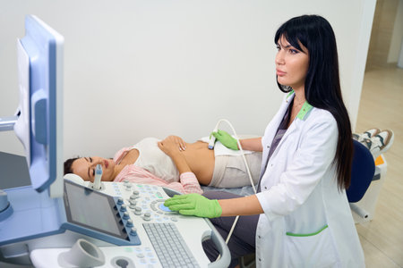 Female gynecologist doing ultrasound examination to young pregnant womanの写真素材