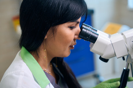 Partial side view of female scientist looking in microscope in laboratory