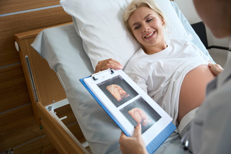 Pregnant woman looking at ultrasound photo of her future baby in hand of doctor