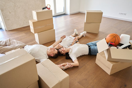 Family holding hands and dreaming on floor in new modern townhouse during moving