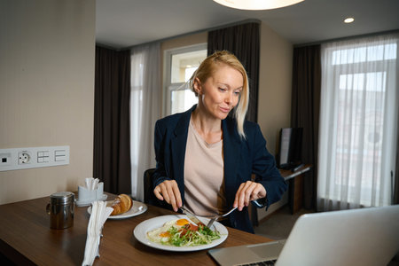 Female entrepreneur reading something on laptop in suite over brunchの写真素材