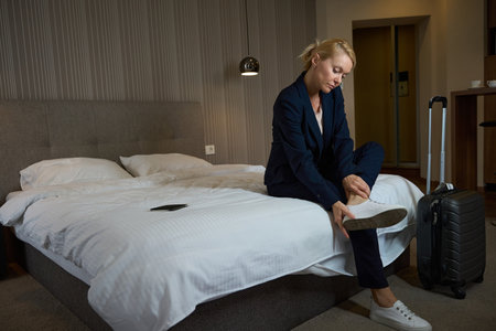 Businesswoman pulling sneakers off tired feet upon arrival at suiteの写真素材