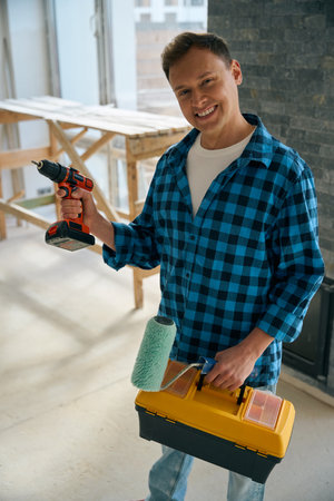 Smiling man standing in room and holding different toolsの写真素材