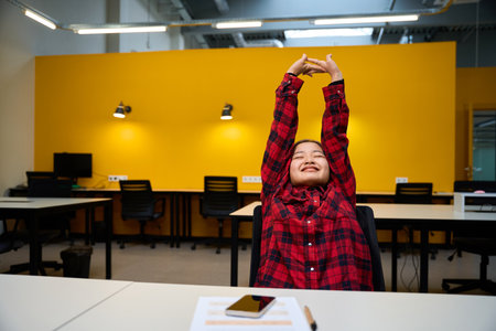 Young smiling asian female IT employee stretching during break at desk in office