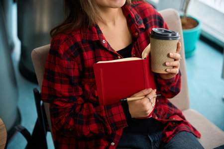 Focus on foreground of partial female IT employee with coffee cup and notebookの写真素材
