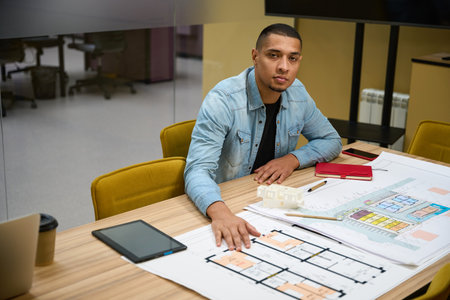 Tired young man sitting at table while working with plan