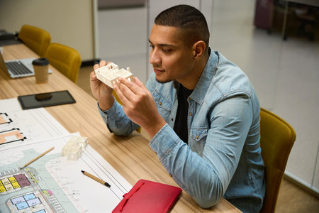 Smiling young male architect sitting and looking at building model