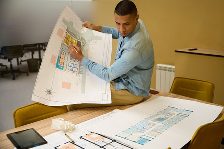 Focused young man sitting on table while writing on blueprint