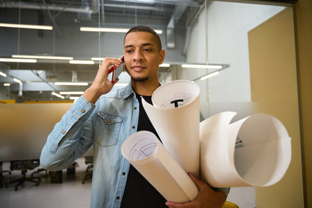 Pleased young male architect standing while talking on phone