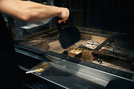 Partial chef waving over fish fillet frying in burning fire place in restaurantの写真素材