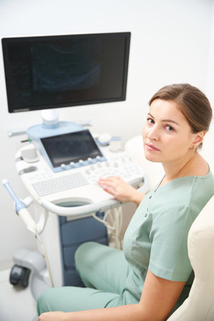 Doctor looking at camera while working on blurred modern ultrasound machineの写真素材