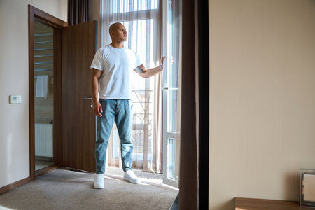 Focused african american man opening door to balcony in hotel room at sunny dayの写真素材
