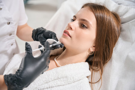 Partial female cosmetologist doing face beauty injection with syringe of womanの写真素材