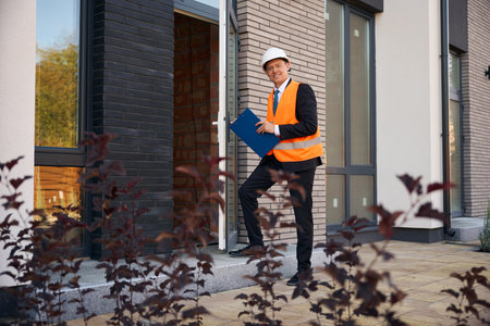 Male engineer wearing helmet and safety vest entering house