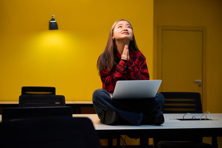 Worried asian female IT employee with praying hands ask hope while using laptop
