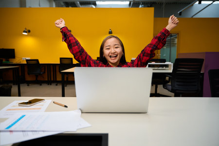 Female IT employee with hands in air celebrating success and watching laptopの写真素材