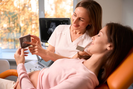Pregnant woman and doctor looking at ultrasound photo in hospital
