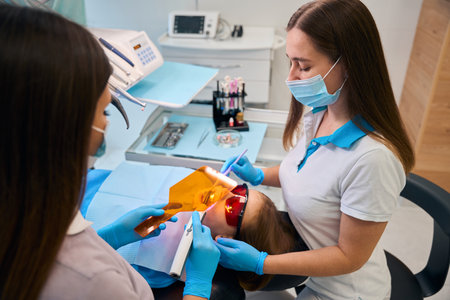 Woman dentist puts a photopolymer filling on a girlの写真素材
