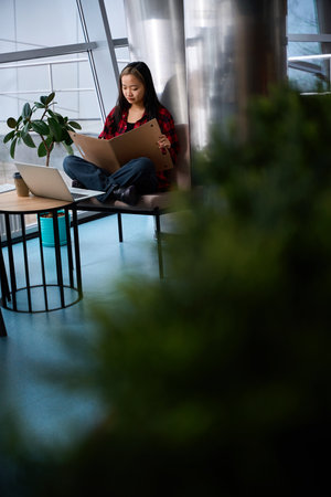 Young asian female IT employee writing in notebook sitting on chair at table